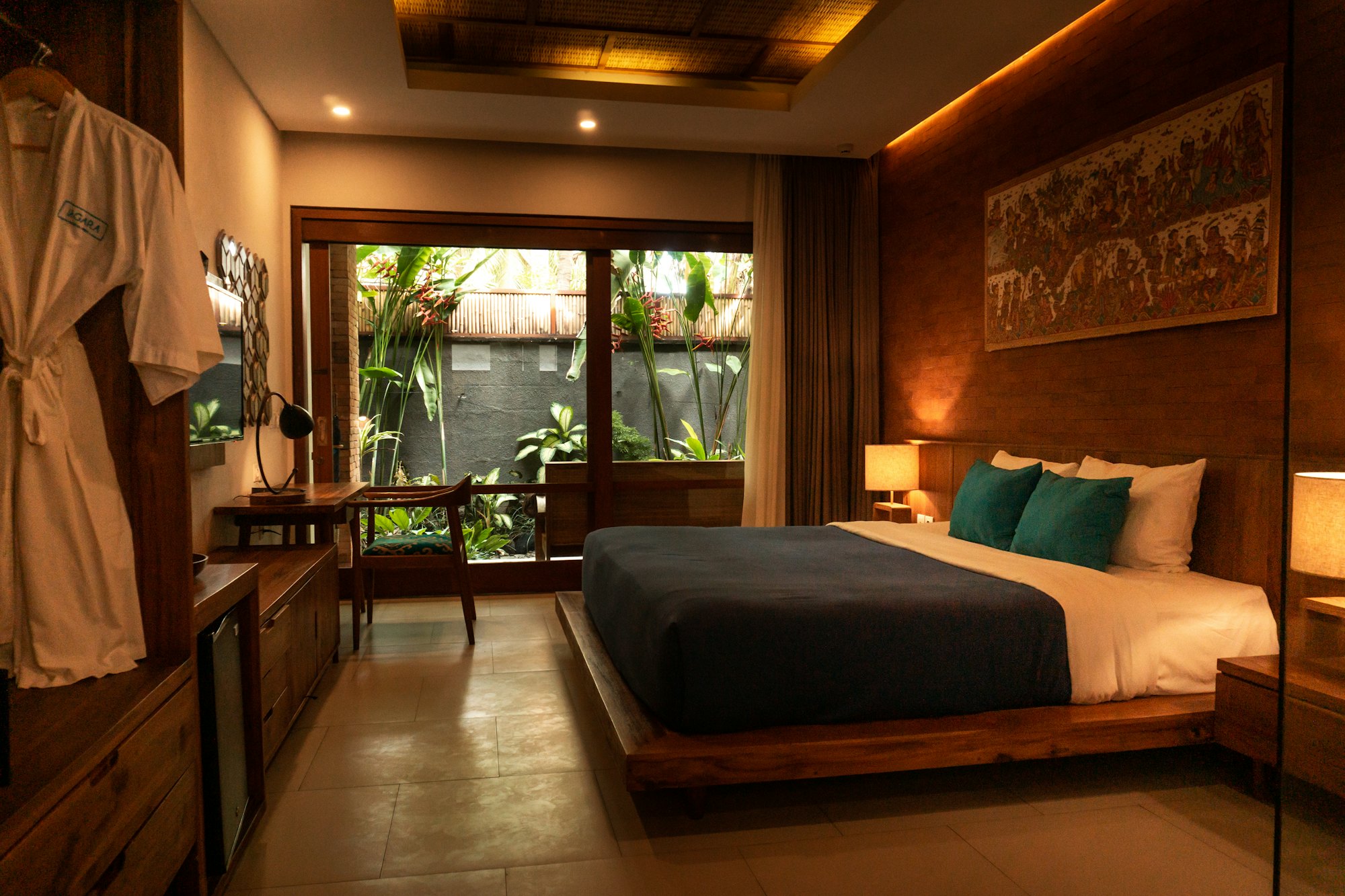 Warm-lit bedroom with dark timber finishes opening onto a garden