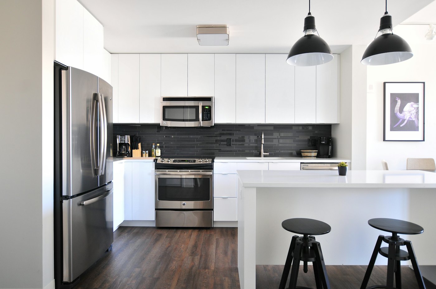 White modular kitchen with an island, black pendant lights and tall appliance units