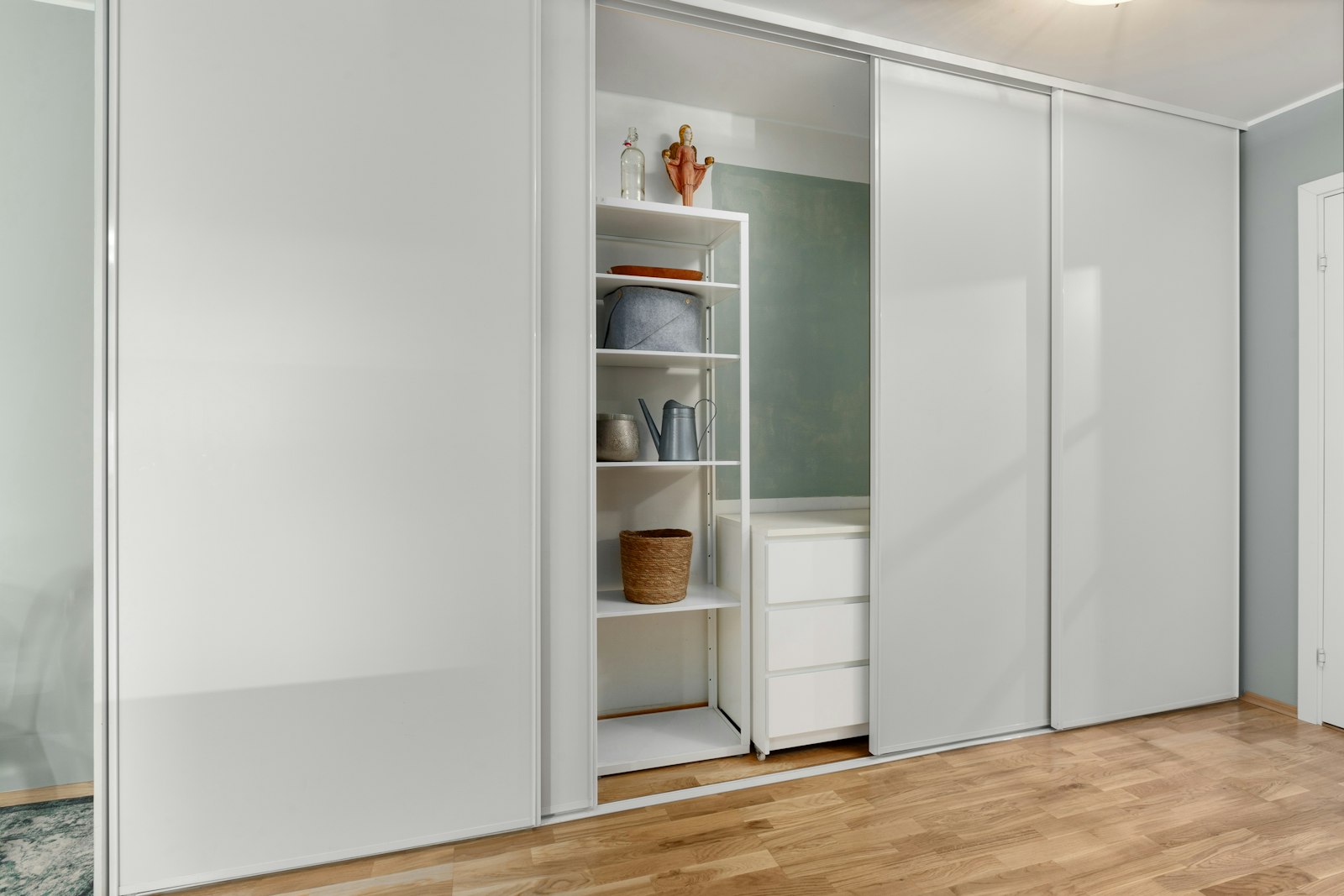 Full-wall sliding wardrobe with white high-gloss acrylic shutters, one opened to show shelving and drawers