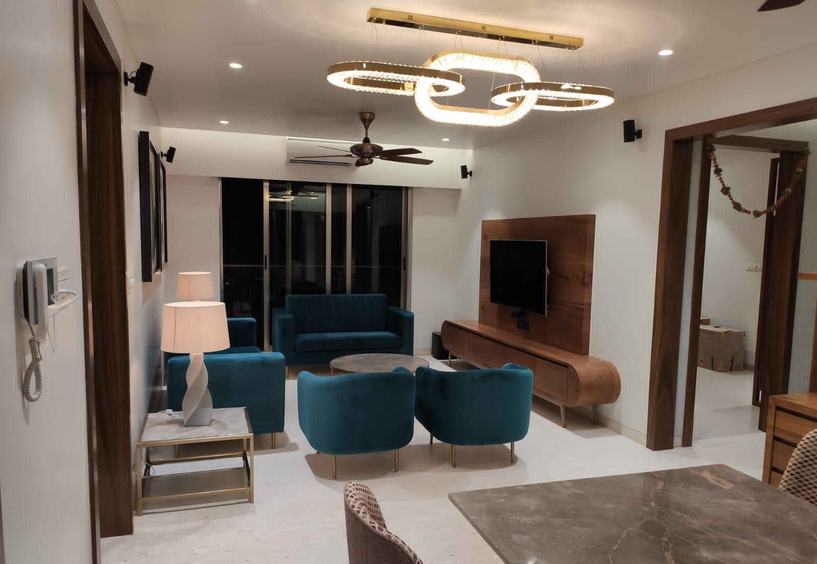 Living room with teal velvet seating, a statement ring light and walnut TV wall